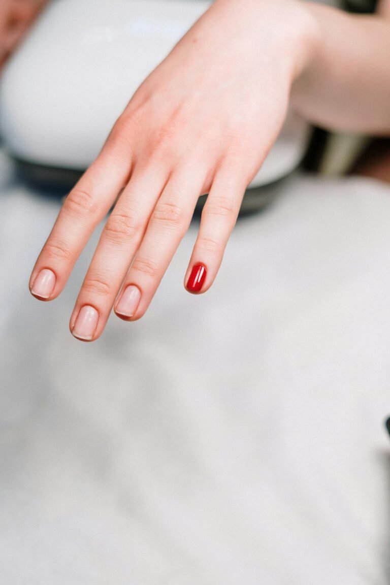 A close-up of a hand with one red painted nail, showcasing a minimalistic manicure style.