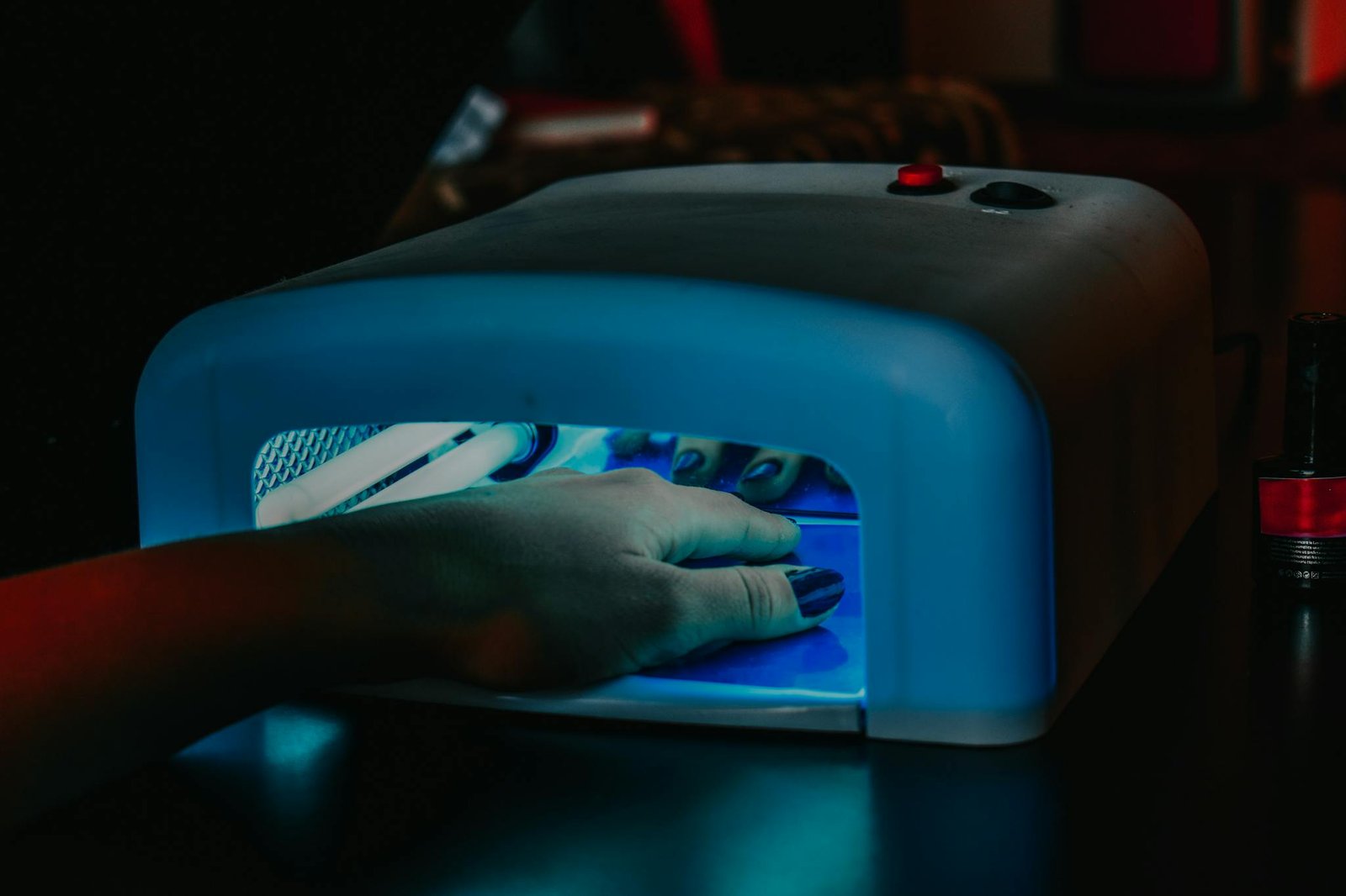 A hand with manicured nails being cured under a blue LED lamp for gel polish.
