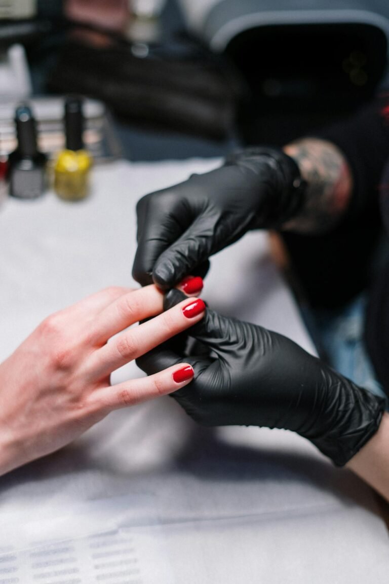 Close-up of a manicurist applying red nail polish in a salon.