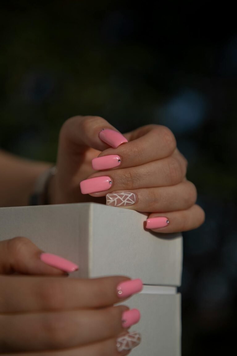 Detailed close-up of hands with pink nail art, holding a white box in an artistic shot.