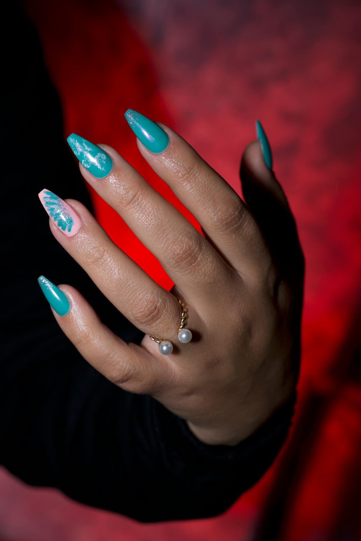 Stylish hand adorned with turquoise and pink nail polish, featuring a pearl ring.