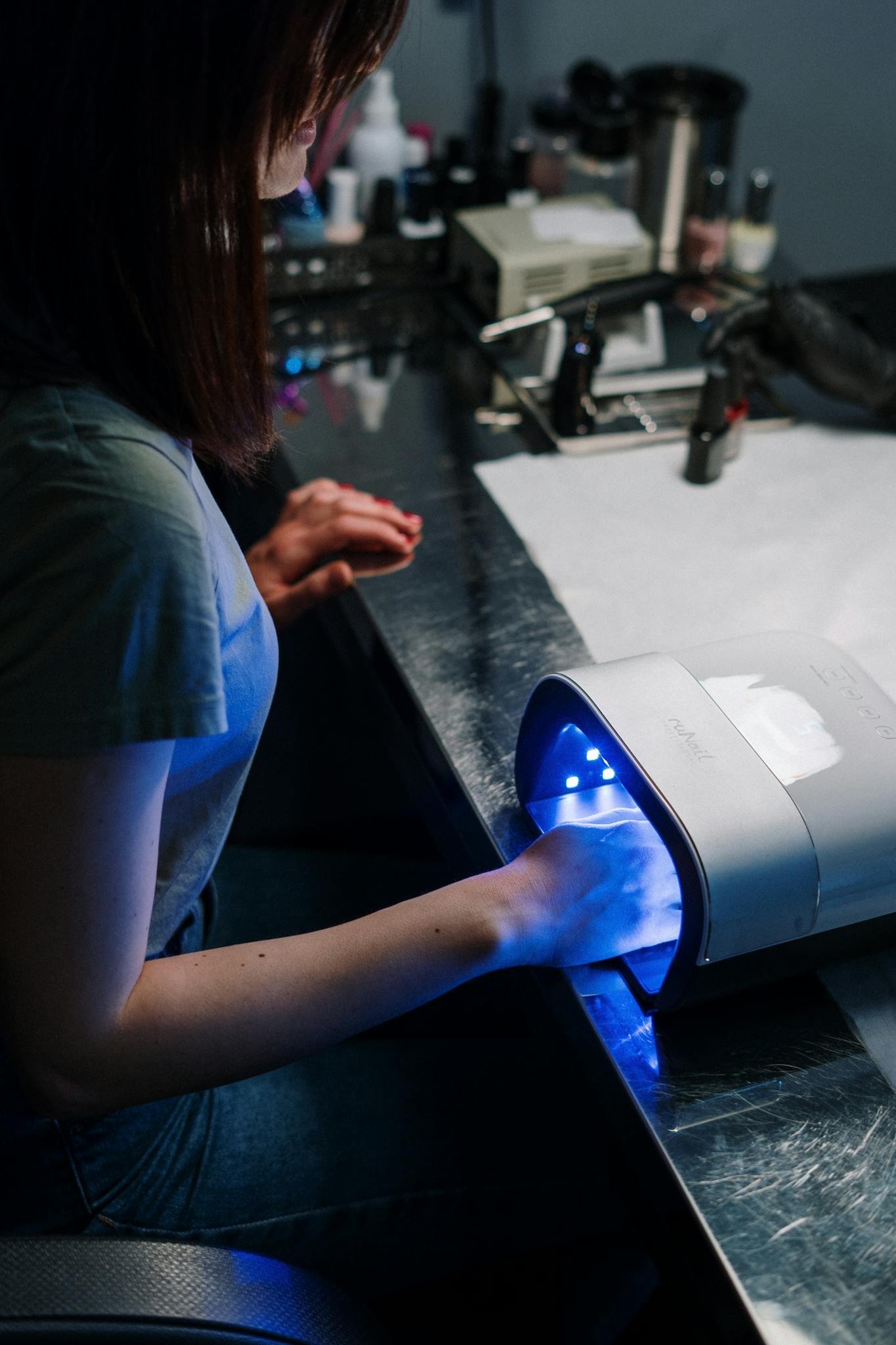 Woman receiving a gel manicure with UV lamp at a nail salon.